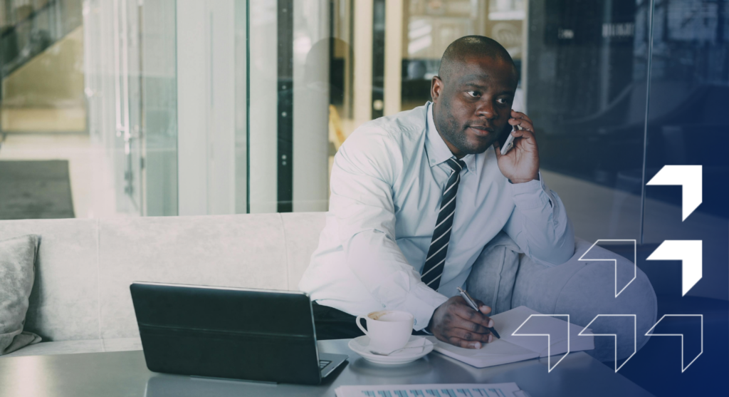 Professional man in business attire on phone call at desk with laptop and coffee cup in modern office setting.