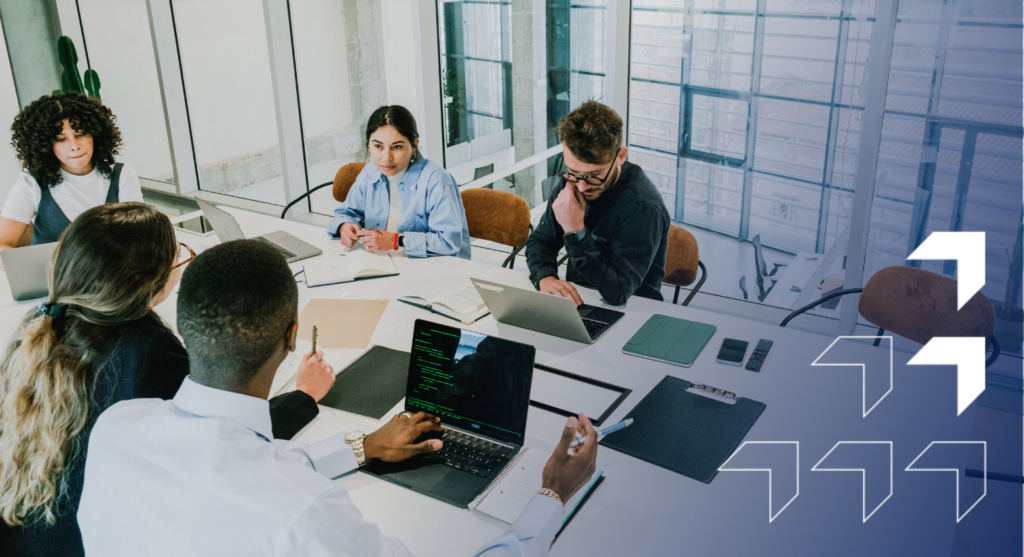 A diverse team of six professionals collaborates around a conference table in a modern office with floor-to-ceiling windows overlooking a city skyline.