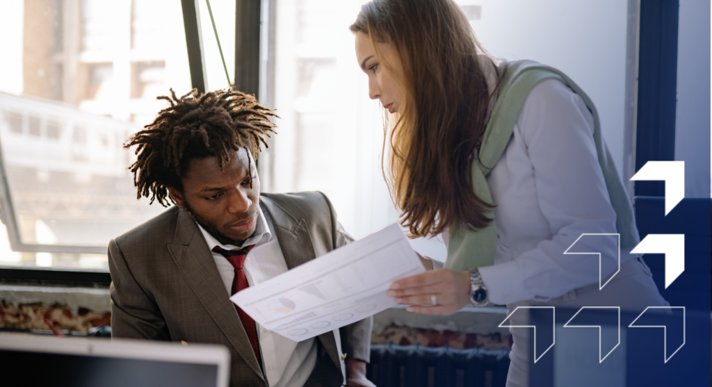 Two business professionals reviewing documents together in a modern office with city views in the background.